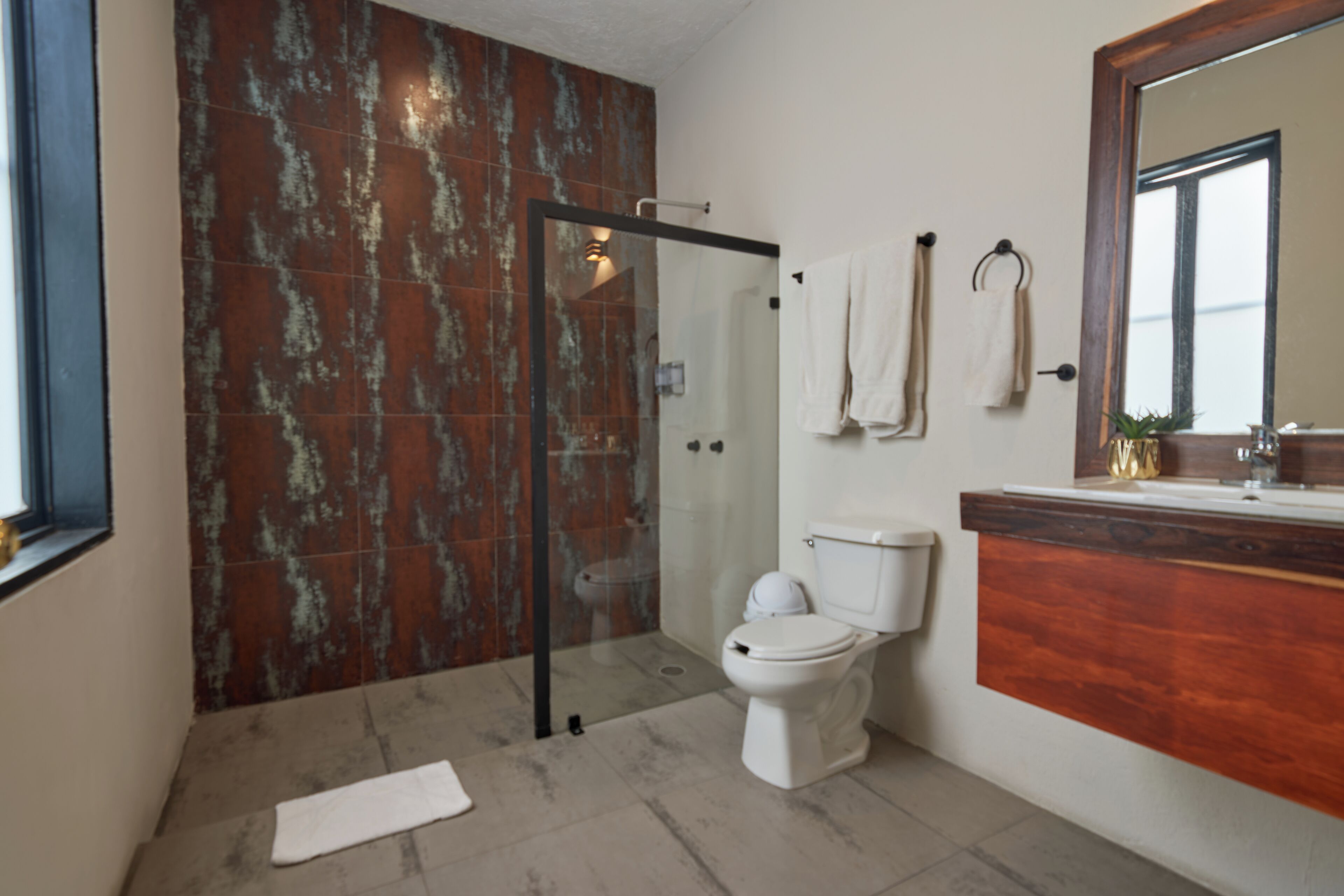 A bathroom with a glass-enclosed shower, a toilet, and a wooden vanity with a mirror.