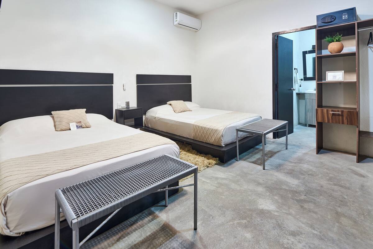 Una habitación de hotel moderna con dos camas, una mesita, un banco y un armario.
