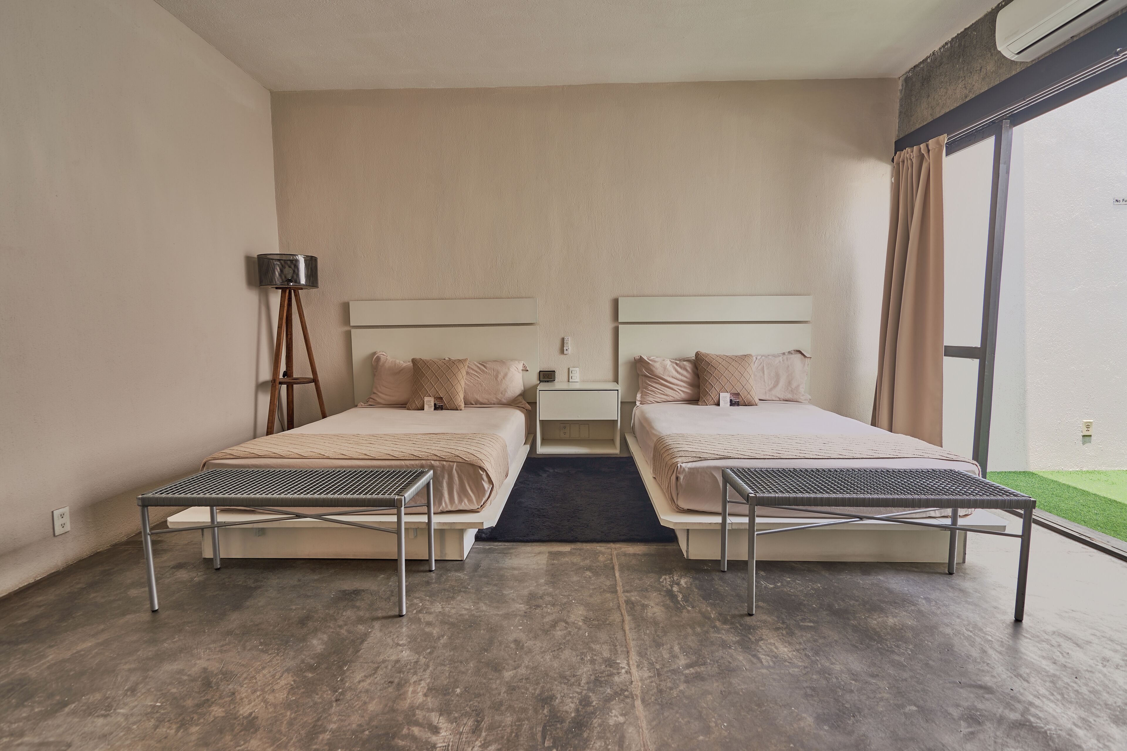 Ein Hotelzimmer mit zwei Betten, einer Stehlampe, einem kleinen Tisch und Blick ins Freie.