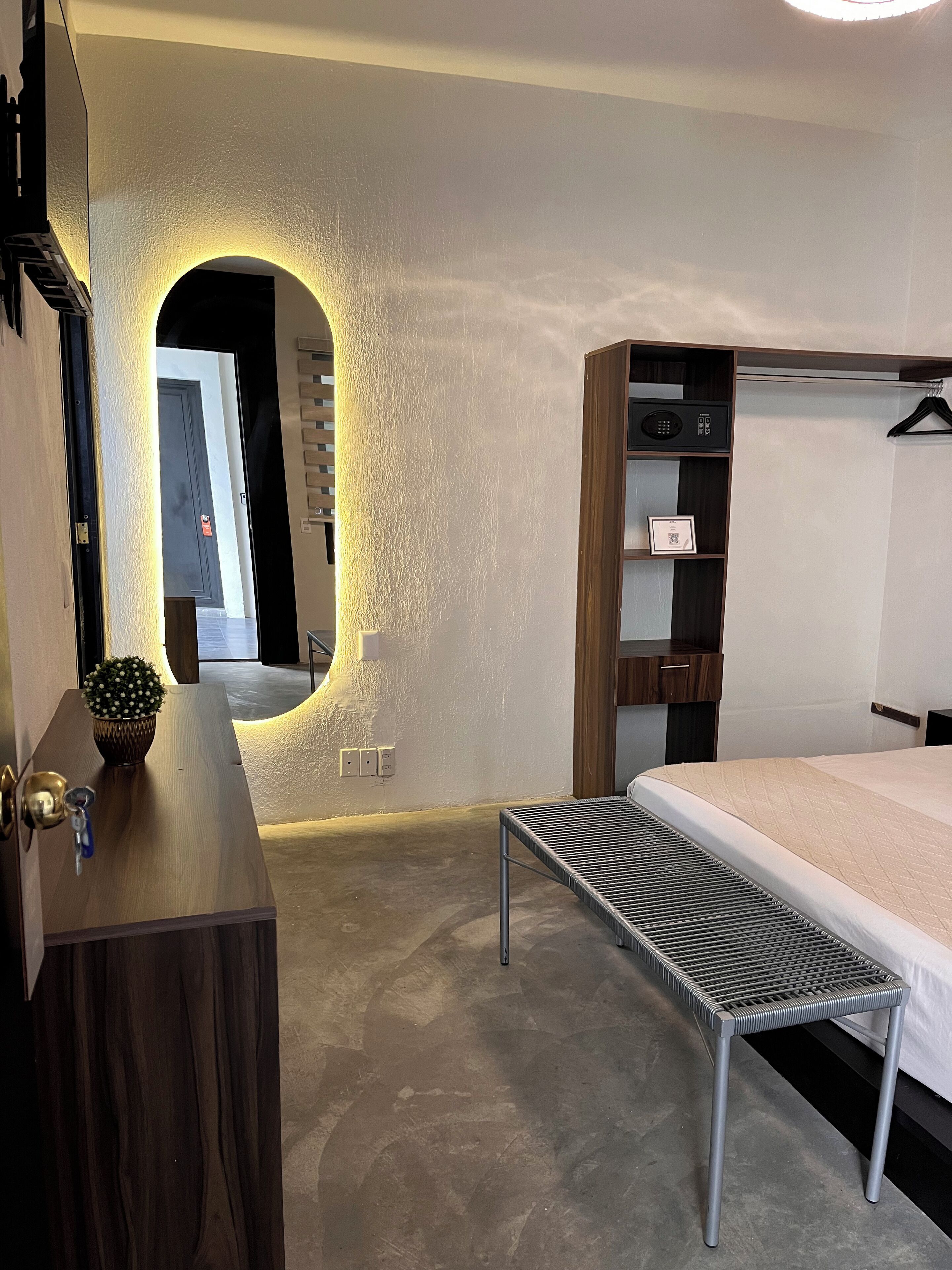 Un dormitorio moderno con una cama, una mesita de noche con lámpara, una planta pequeña y un armario con espejo.
