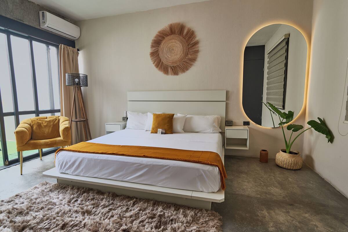 Un dormitorio moderno con una cama grande, un adorno circular en la pared, un espejo y una planta en maceta.