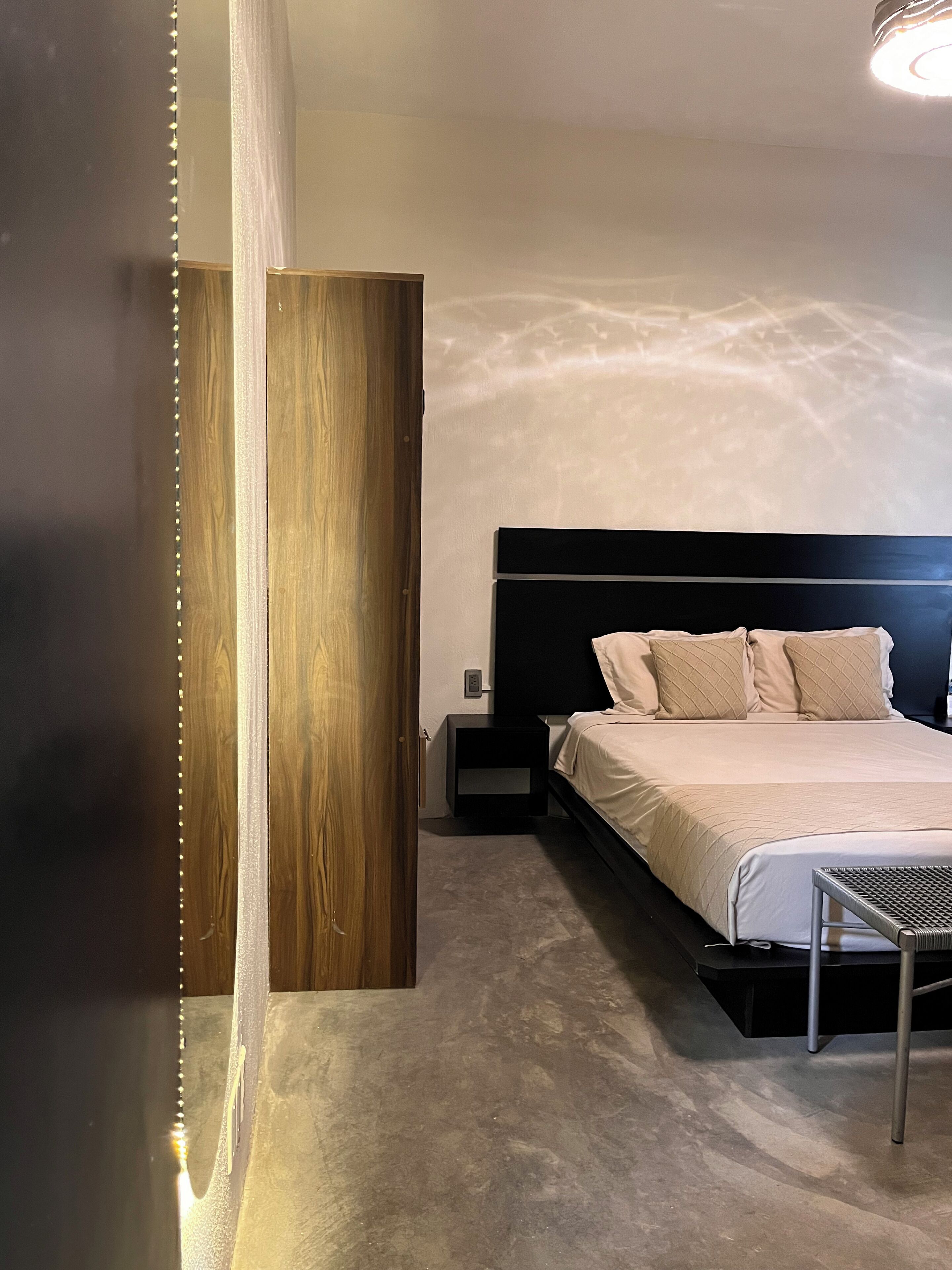 A modern bedroom with a large bed, a nightstand, a wooden panel, and a small table.