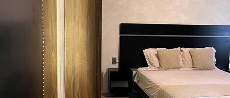A modern bedroom with a large bed, a nightstand, a wooden panel, and a small table.