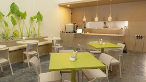 Un restaurante con mesas y sillas redondas, una barra con un cocinero, y un ventanal grande.