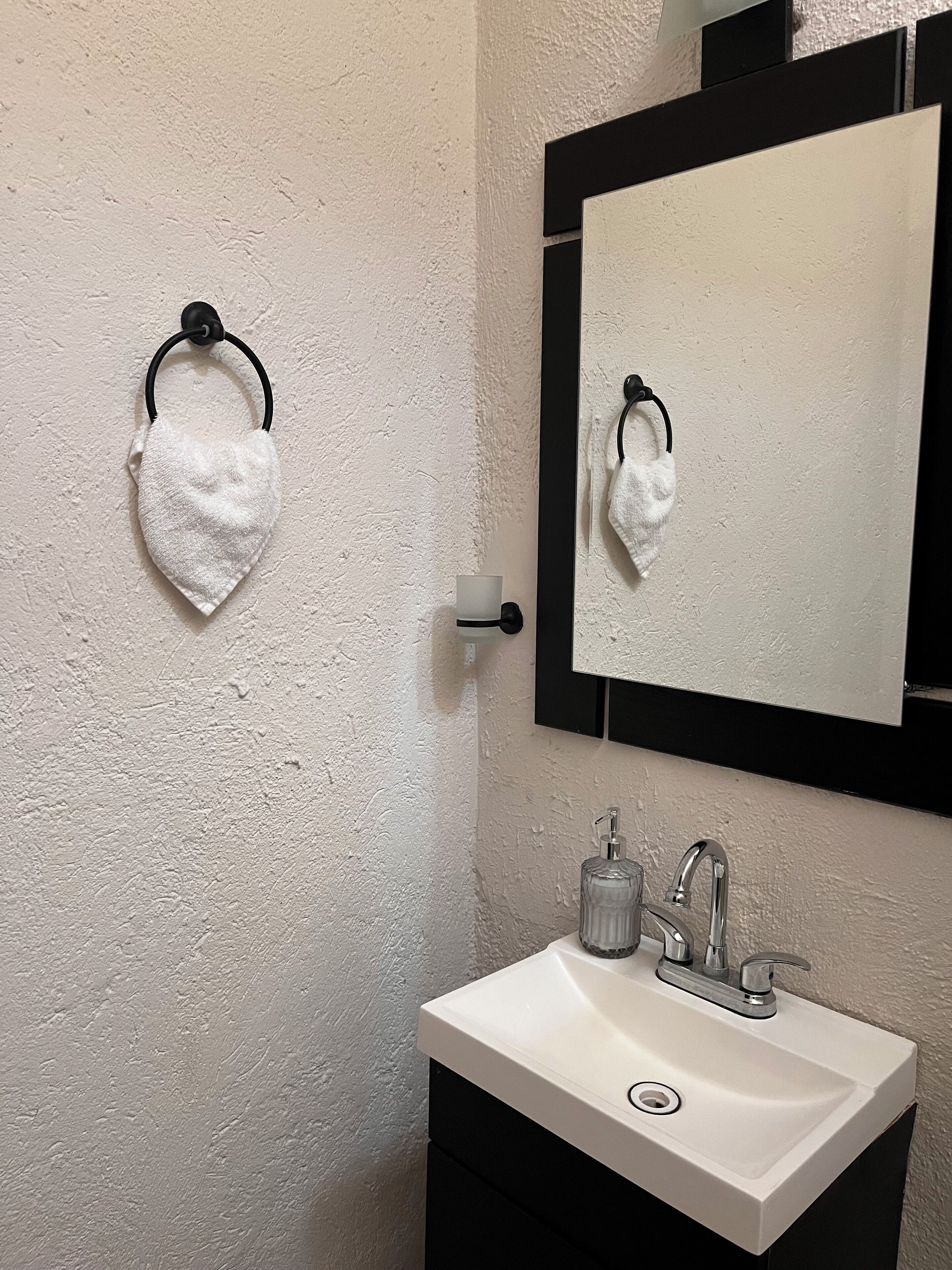 Un baño con un lavamanos blanco, un espejo y dos toallas blancas colgadas en ganchos.