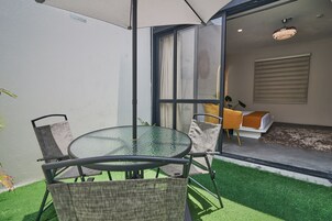 Un porche acristalado con una mesa redonda y sillas, una pequeña silla amarilla y una ventana con cortinas.