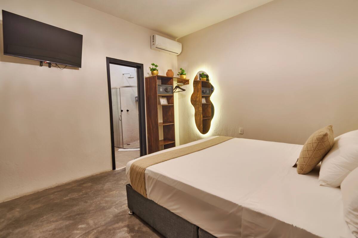 Un dormitorio con cama, televisor montado en la pared, armario y espejo con repisas.