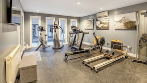 Et fitnesscenter med træningsudstyr, store vinduer og kunst på væggene.
