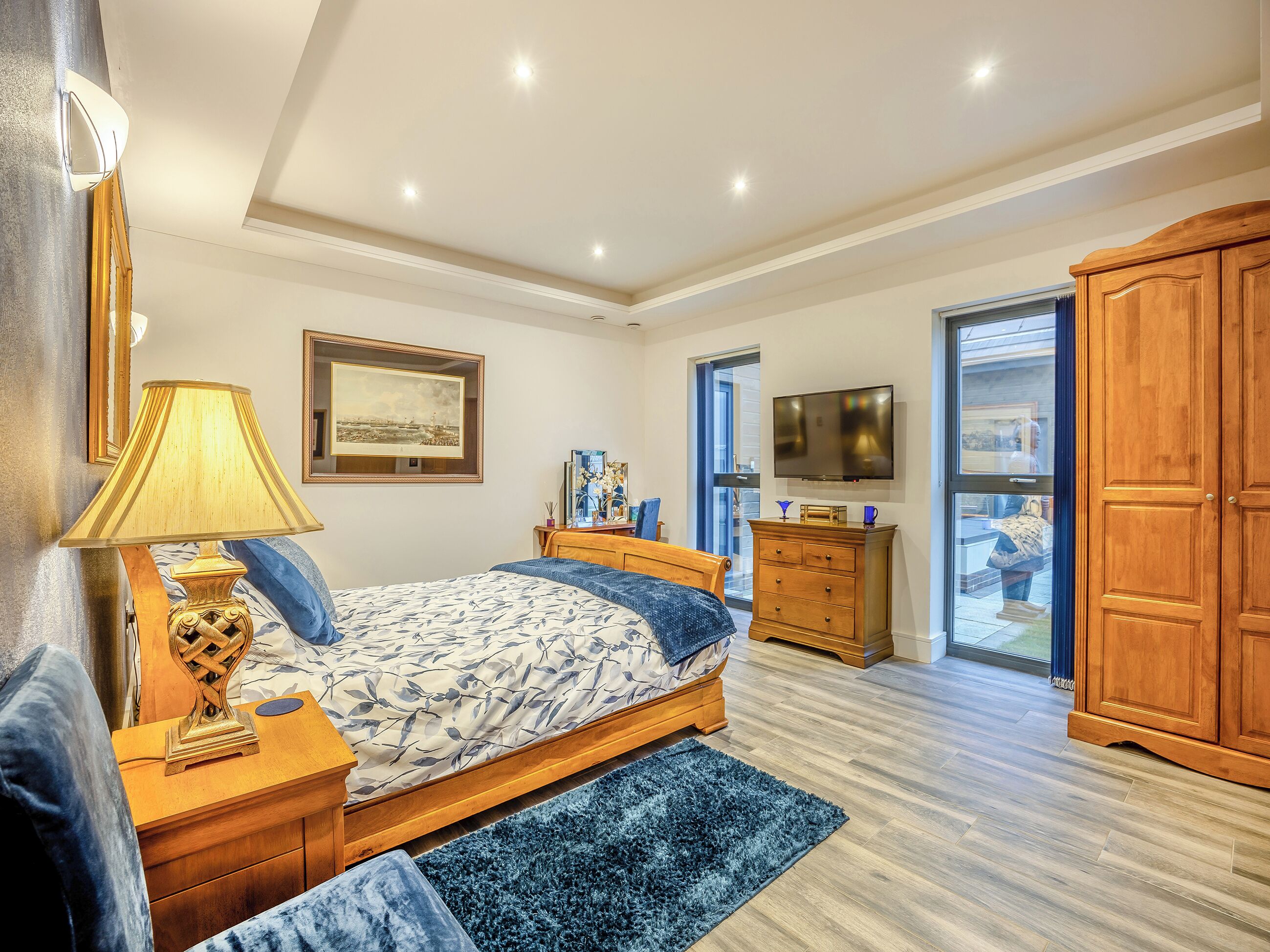A bedroom with a bed, bedside table, lamp, dresser, TV, and a large wardrobe.