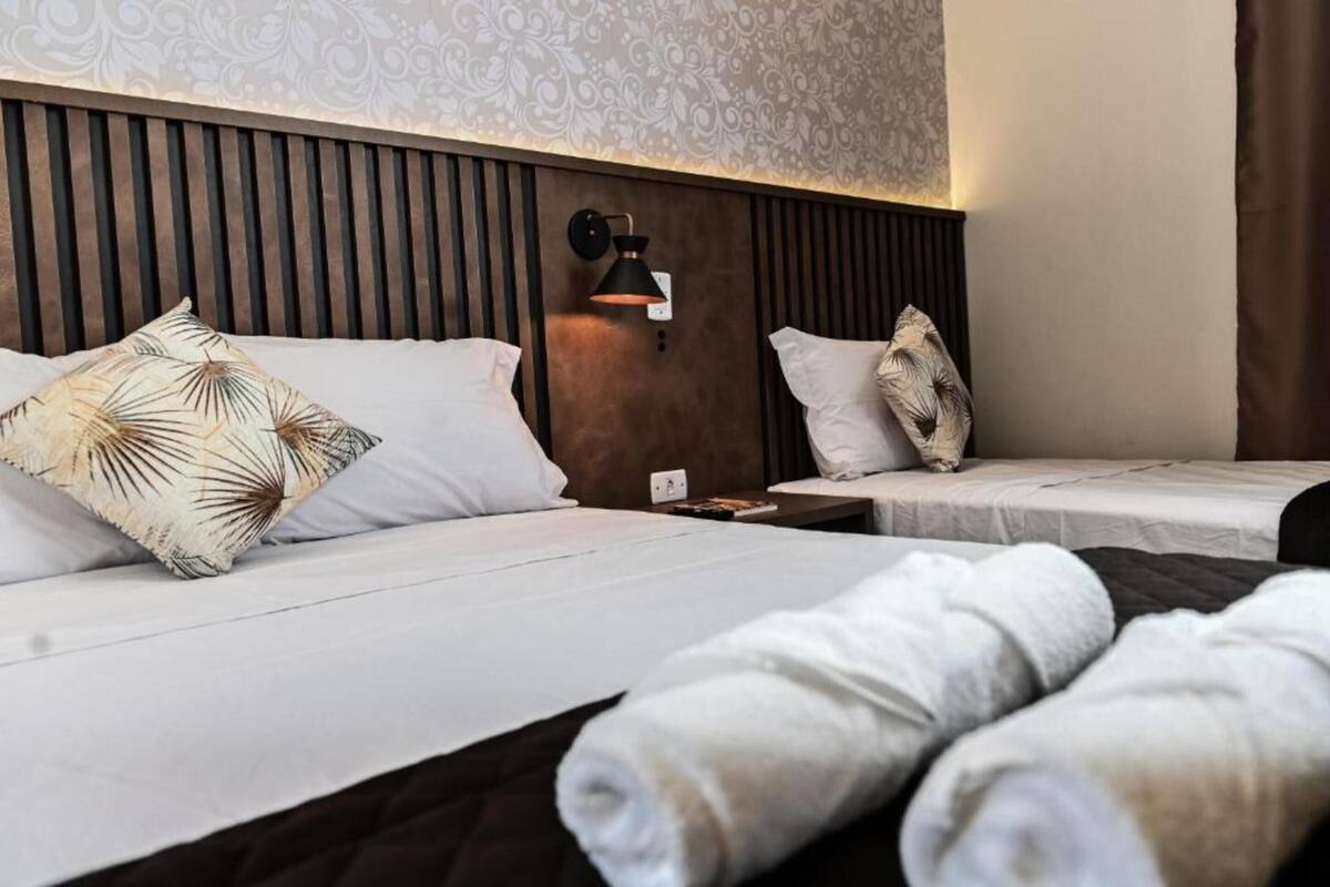 A hotel room with two beds, a wooden headboard, a wall-mounted lamp, and a patterned wallpaper.