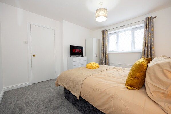 A bedroom with a bed, a TV displaying 'NETFLIX', a window with curtains, and a door. - Captivating 3-bed House in Blackburn (Blackburn)