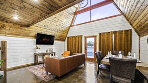 A cozy, wooden-paneled room with a large TV, a dining table, and a comfortable seating area. - Little Woods- Luxury A-frame cabin |Firepit|Hottub (Broken Bow)