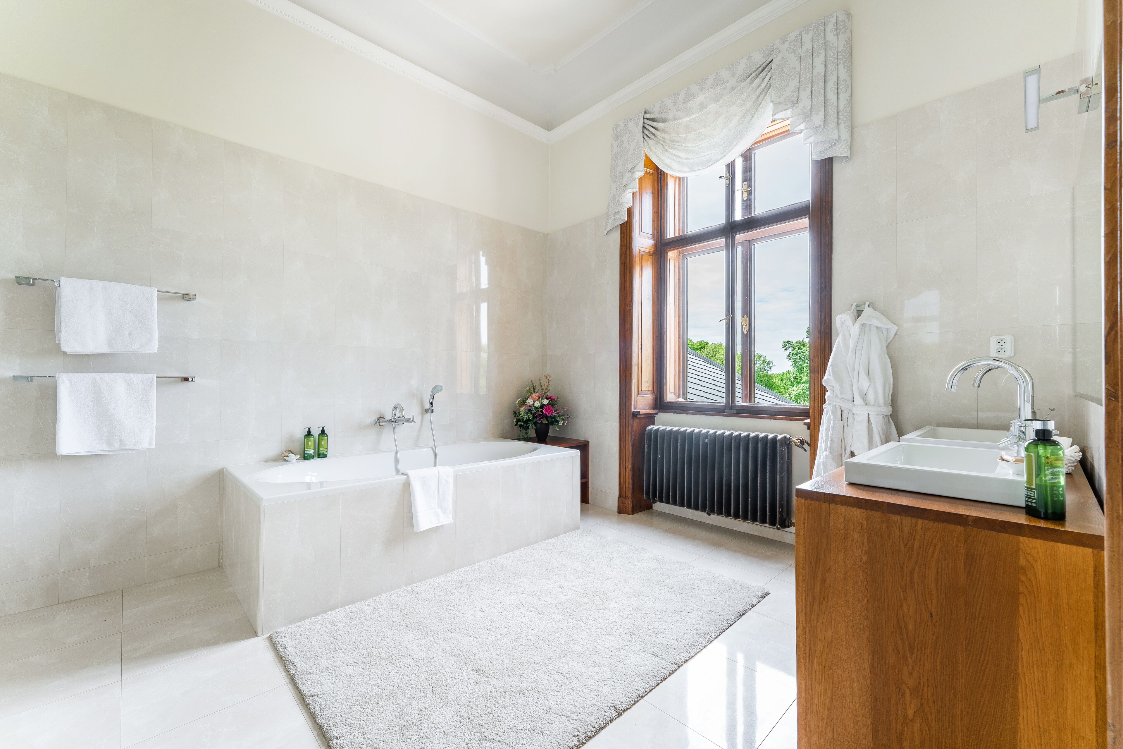 Un baño moderno con una bañera grande, un lavamanos independiente y un ventanal con cortinas.