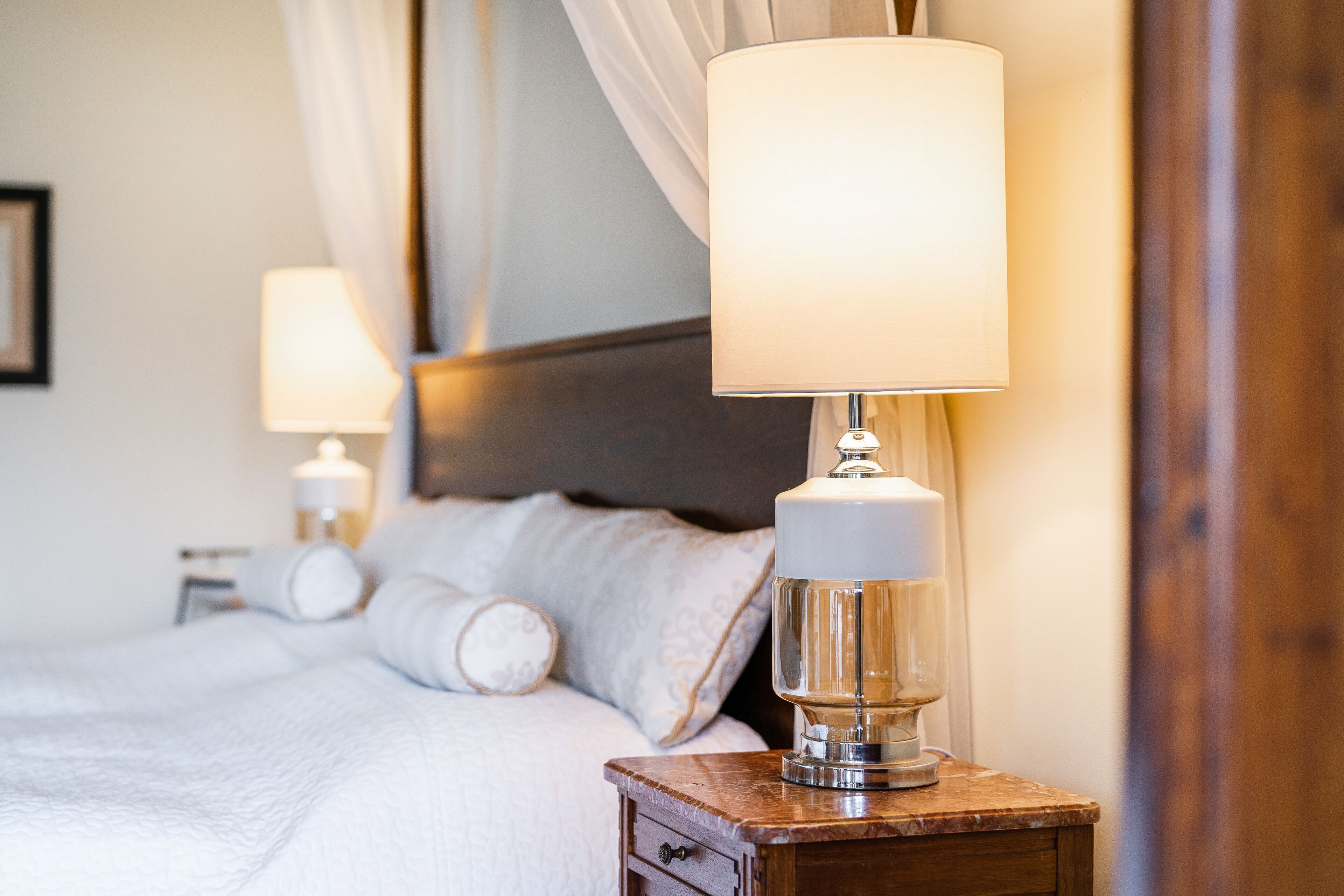 Una cama bien hecha con sábanas blancas y una mesita de noche de madera con una lámpara.