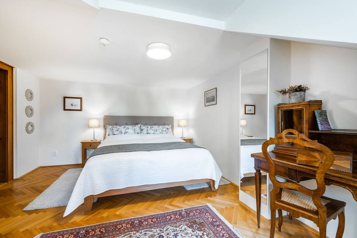 A bedroom with a bed, bedside tables, a desk, a chair, and a rug.