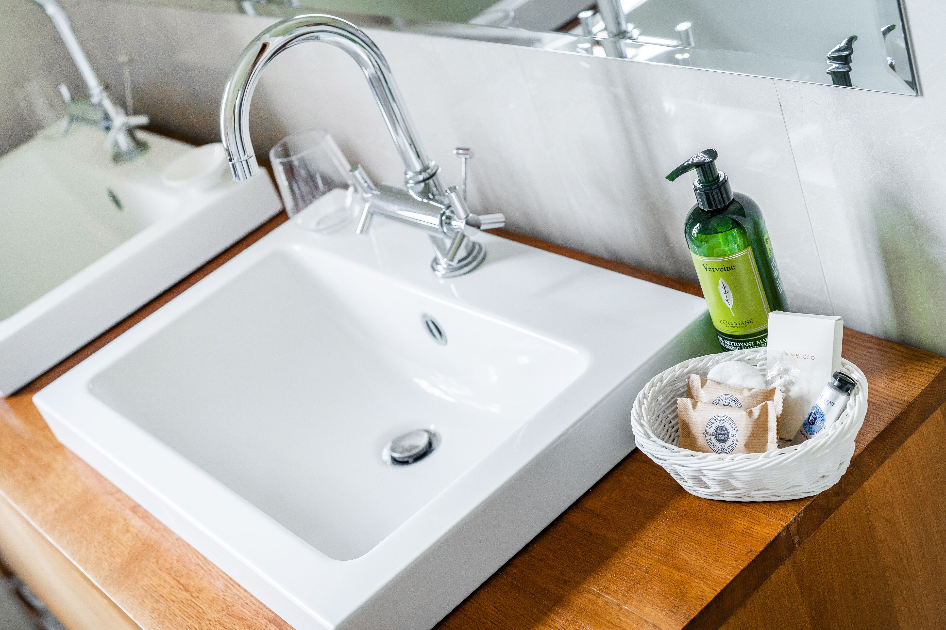Ein Badezimmerwaschbecken mit einem Chrom-Wasserhahn, einem Glas und einem Korb mit Toilettenartikeln.