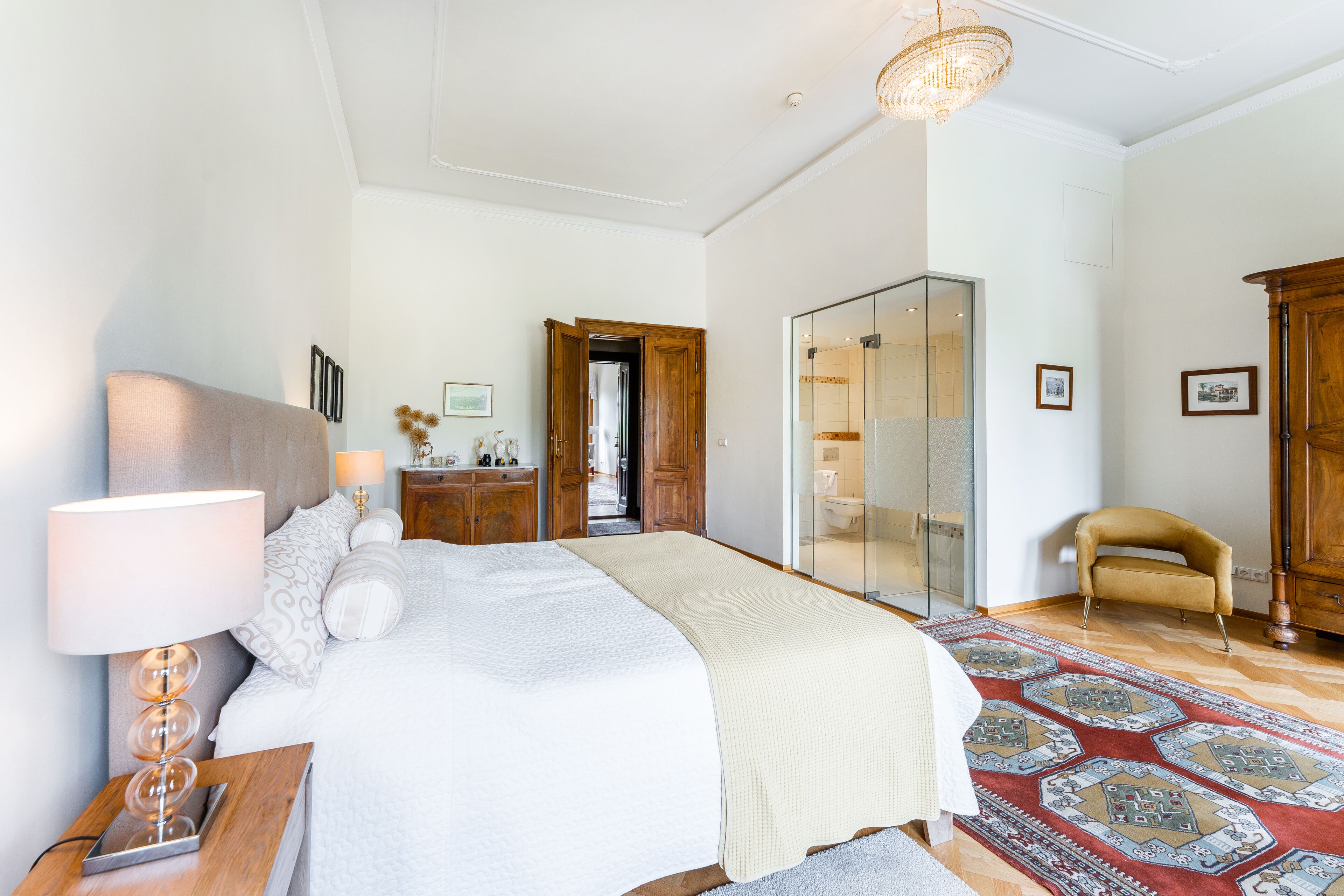 A spacious bedroom with a large bed, bedside tables, a wardrobe, and a glass-enclosed bathroom.