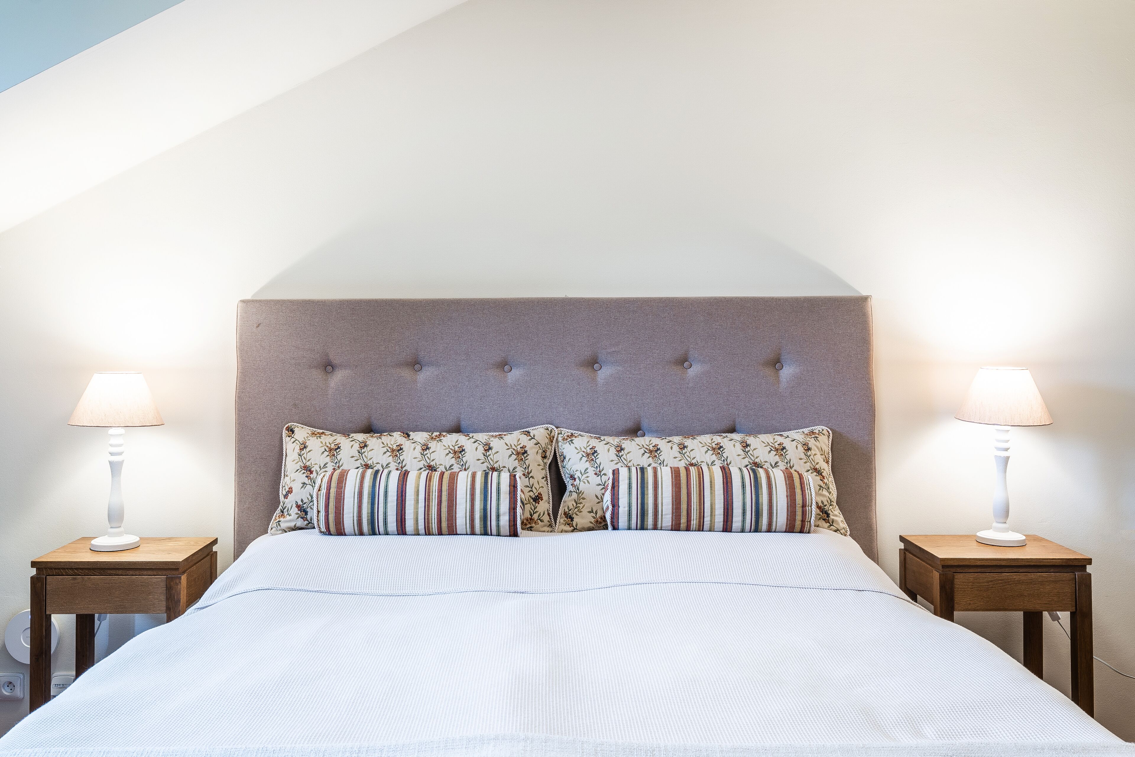 A neatly made bed with a tufted headboard, two bedside tables with lamps, and a floral-patterned pillow.