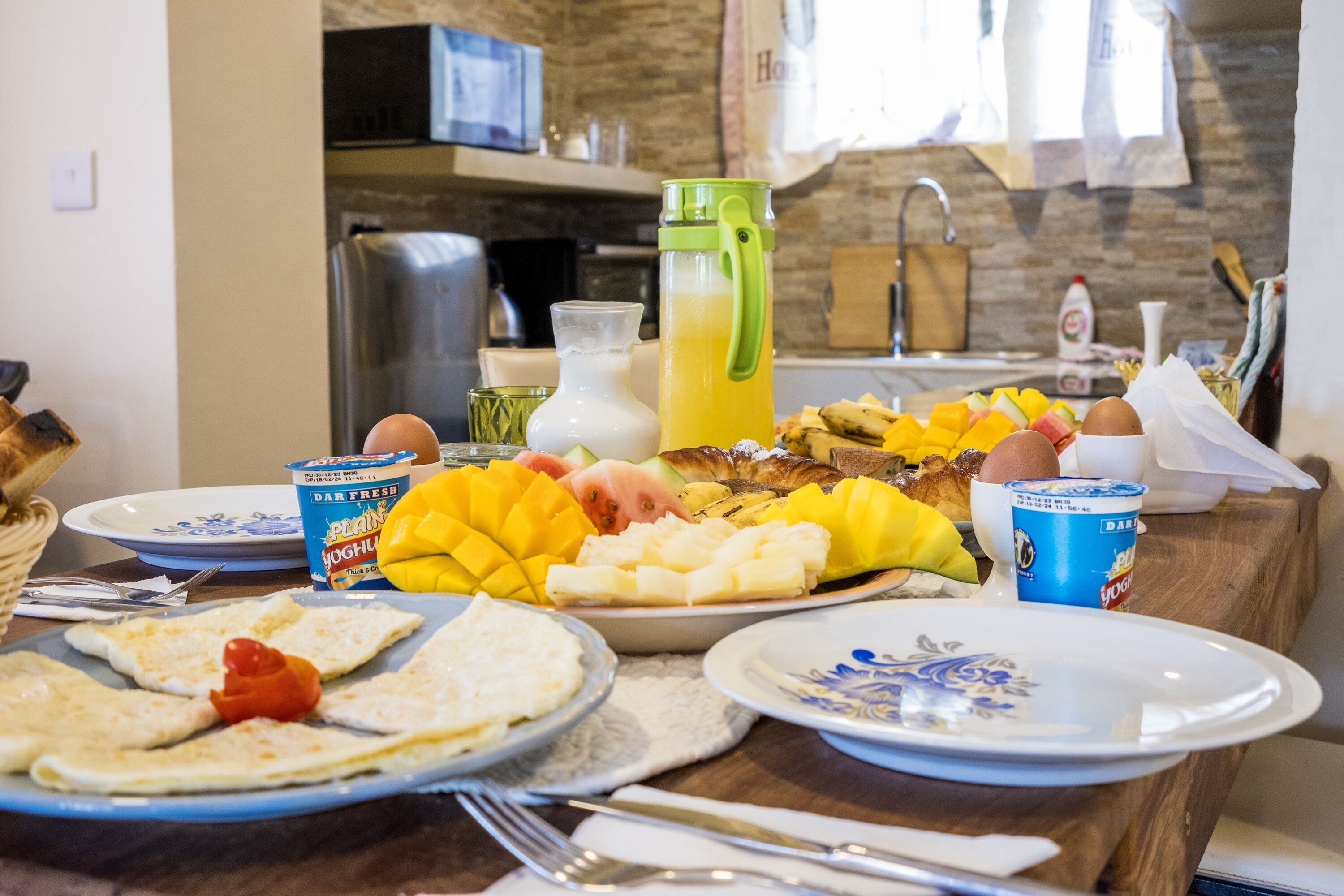 A breakfast table with plates of food, a green water bottle, and a carton of yogurt.