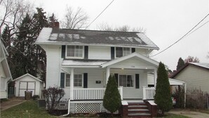 A two-story house with a front porch, a garage, and a small front yard. - Heart of the Falls! Cozy for 2, Spacious for 8, Close to everything! (Cuyahoga Falls)