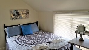 A neatly made bed with a patterned bedspread, a bedside table with a mirror, and a painting on the wall. - Heart of the Falls! Cozy for 2, Spacious for 8, Close to everything! (Cuyahoga Falls)