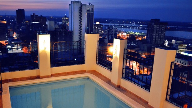 A rooftop pool with a city view, surrounded by high-rise buildings and illuminated windows. - hotel manduara (Asunción)