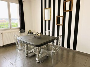 Uma sala de jantar com mesa e cadeiras, uma janela com cortinas e paredes listradas com espelhos.