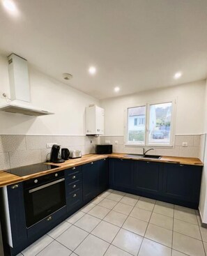 Uma cozinha compacta com armários azul escuro, bancada de madeira, forno embutido e janela com vista.