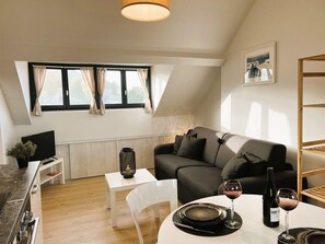 Una habitación moderna y bien iluminada con una mesa de comedor lista para dos personas, un sofá y un televisor sobre un mueble.