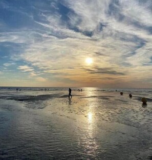 Uma praia com pessoas caminhando, o sol se pondo e céu claro.