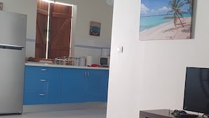 A living room with a sofa, a coffee table, a TV, and a kitchen area with blue cabinets and a wooden door.