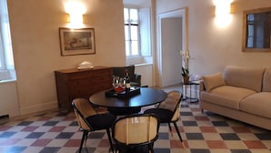 Een woonkamer met een ronde tafel, twee stoelen, een bank, een klein bijzettafeltje met een plant en een houten kast.