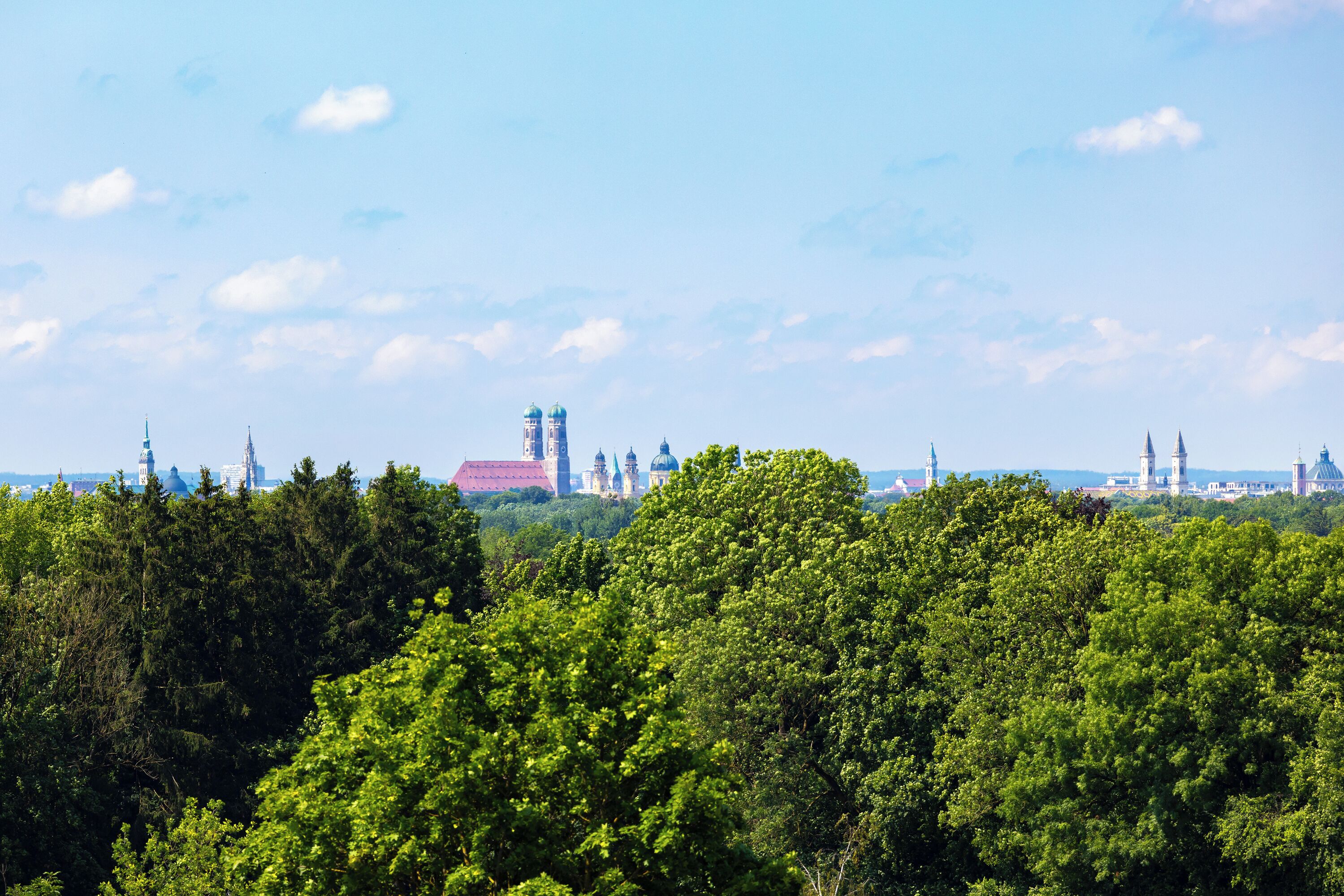 Blick auf eine Stadtlandschaft mit einem markanten Gebäude, das mehrere Kuppeln und Türme aufweist, umgeben von üppigem Grün.