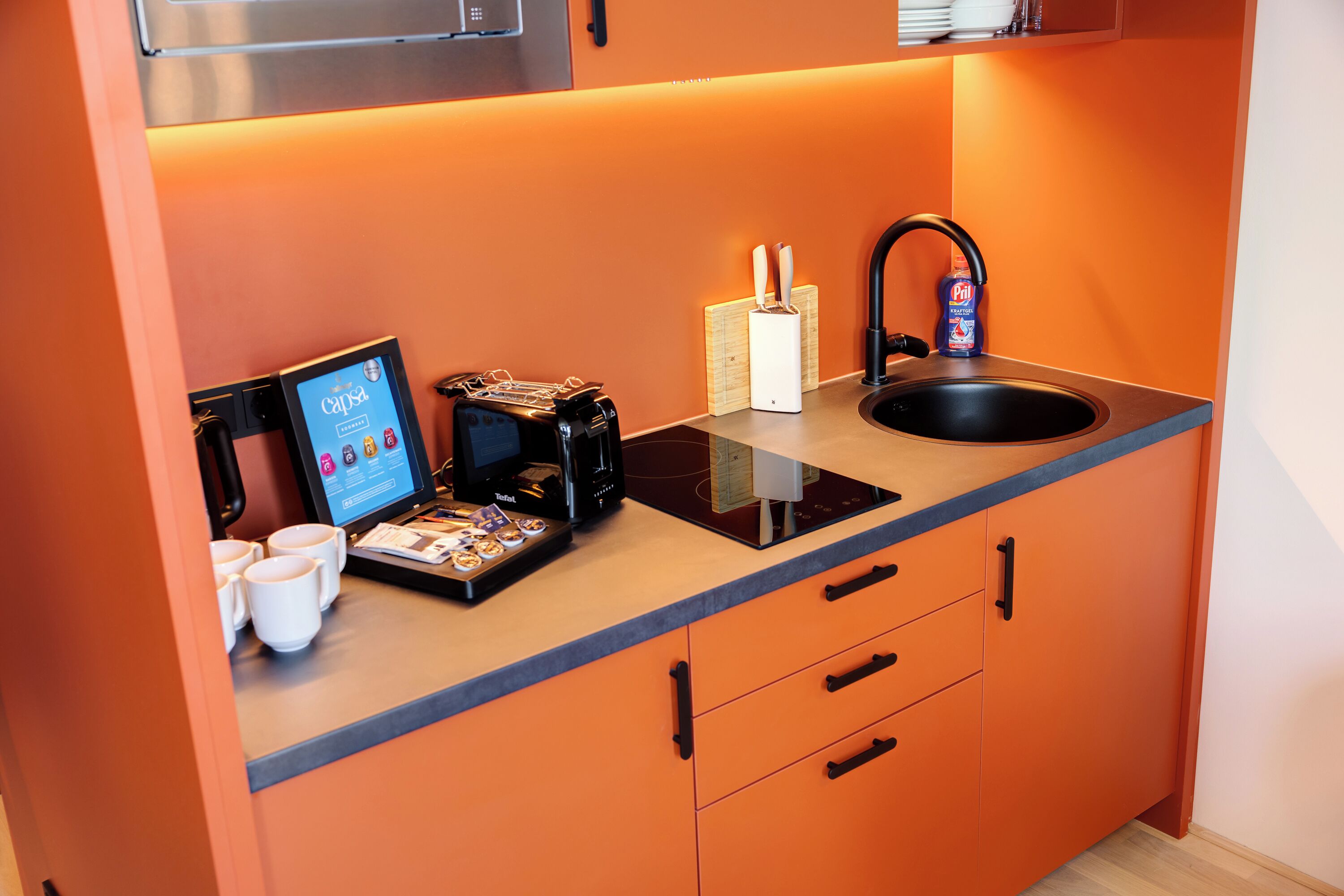A compact kitchen with a coffee machine, a sink, and a digital coffee ordering station.
