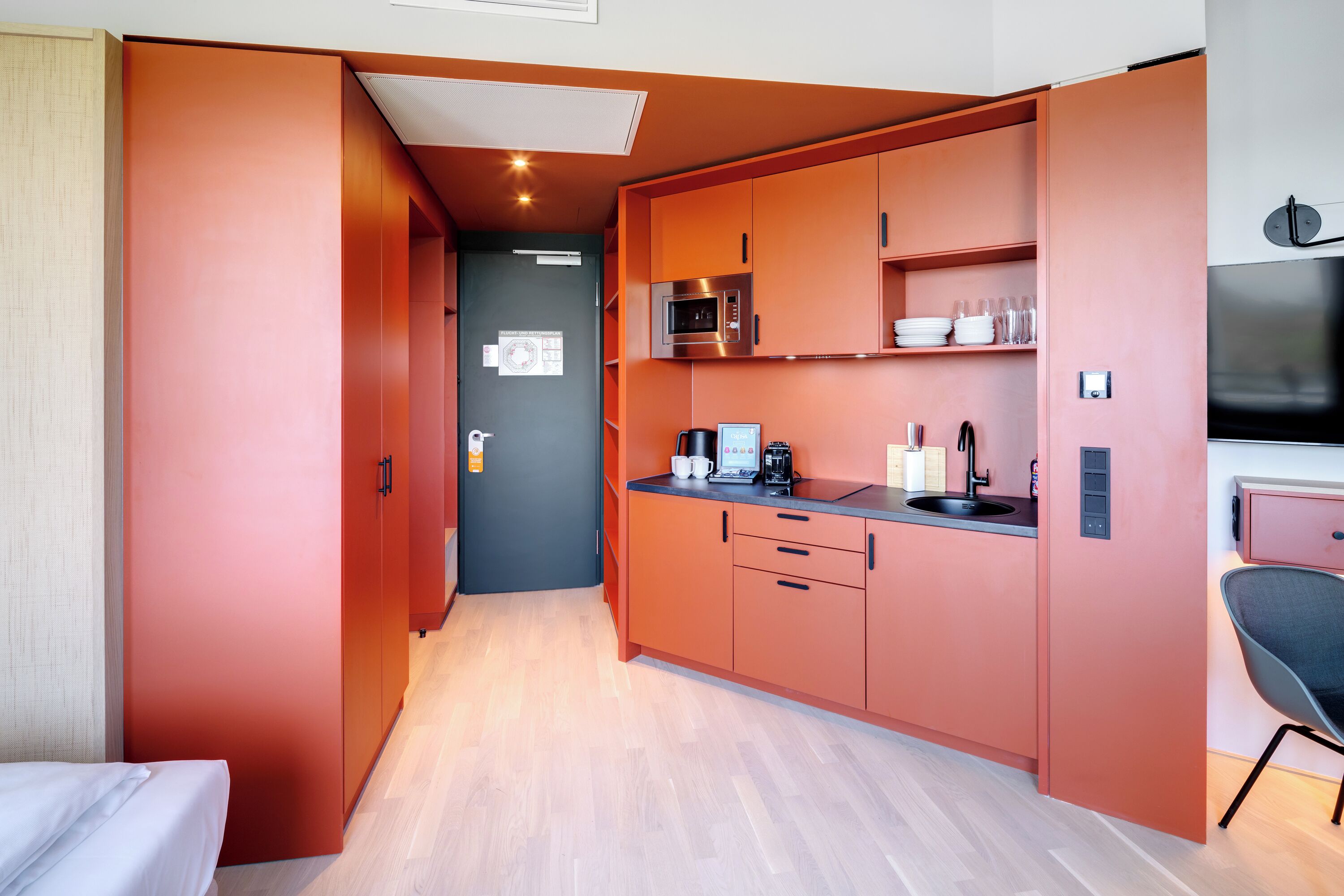 A compact kitchen with orange cabinetry, a microwave, a coffee maker, and a sink.