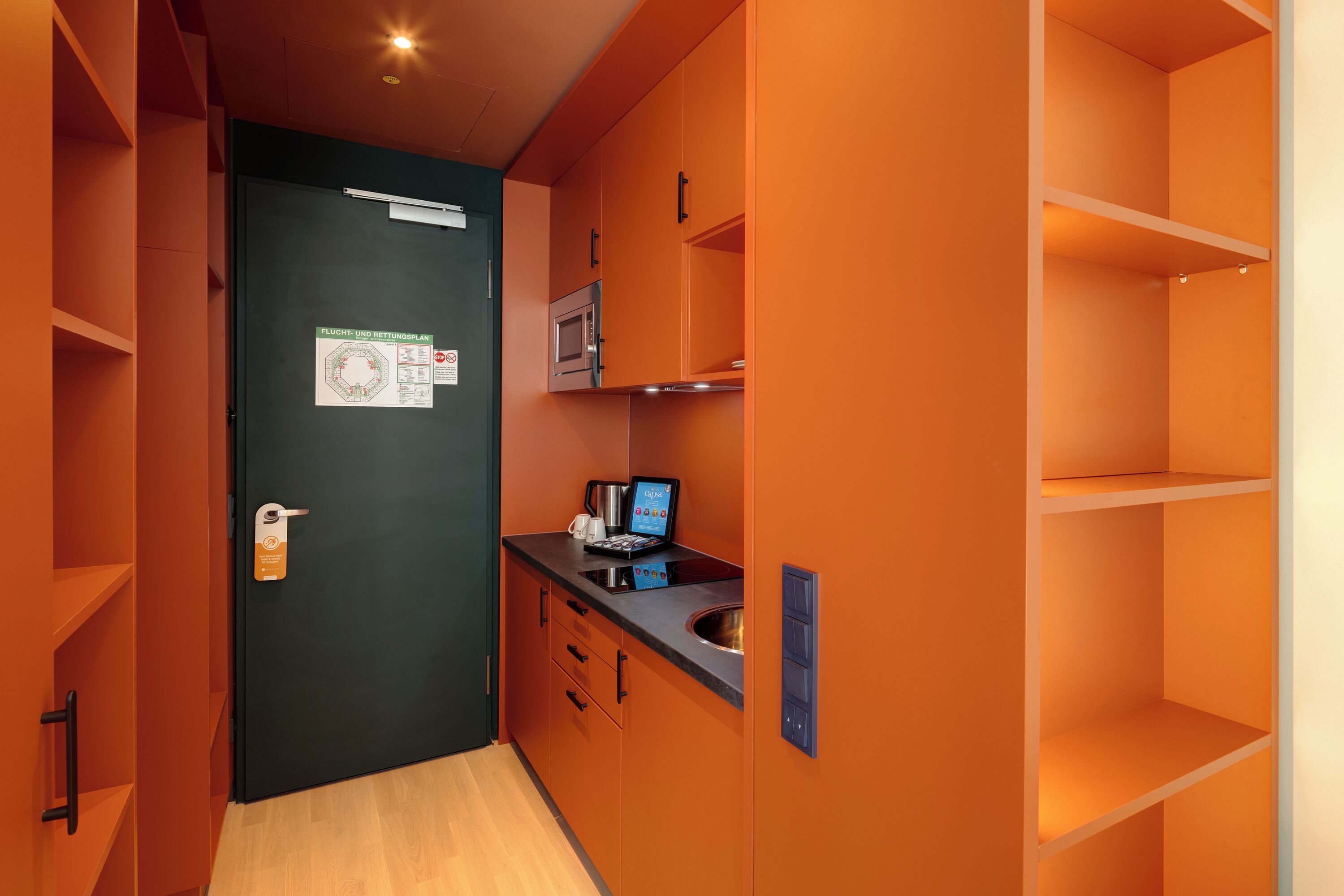 A compact kitchen with a microwave, a digital scale, and a coffee maker on the counter.