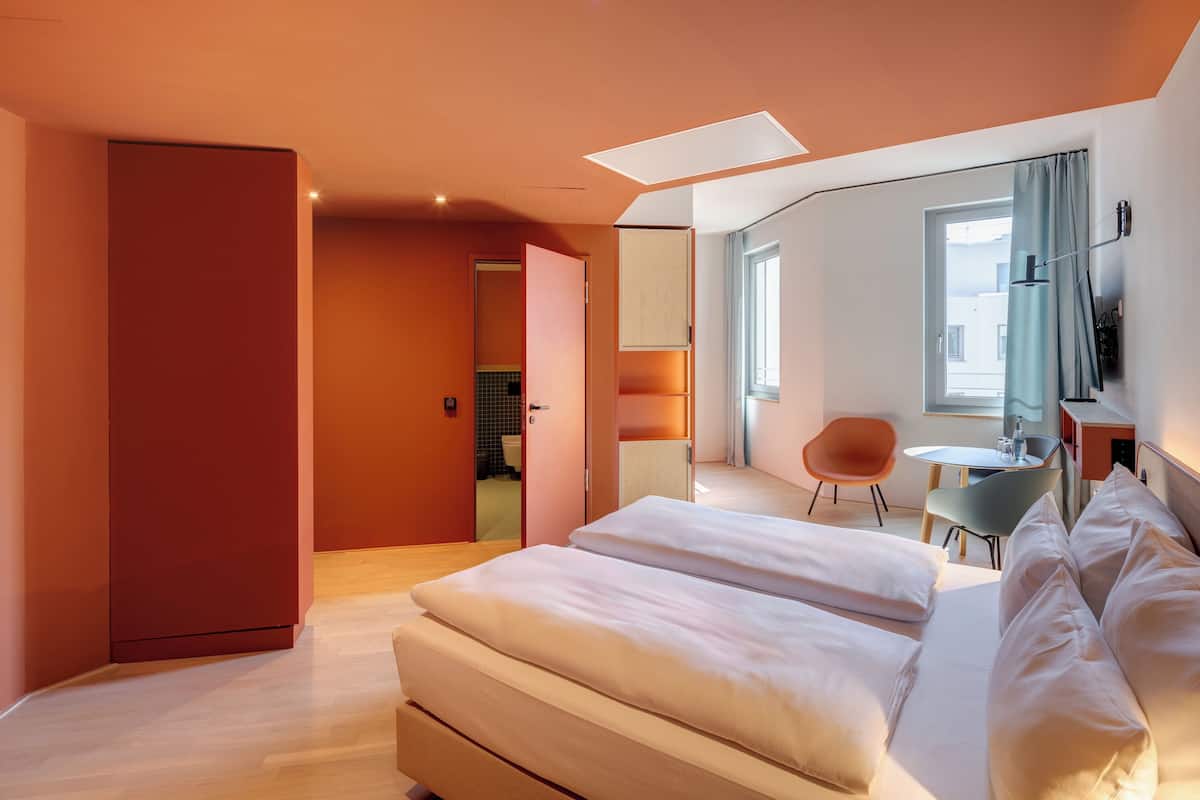 A modern hotel room with a large bed, a desk, and a chair.