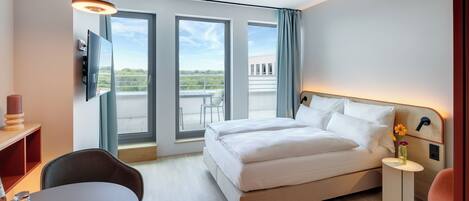 Una habitación de hotel moderna con cama, escritorio, silla, televisor y balcón con vistas.