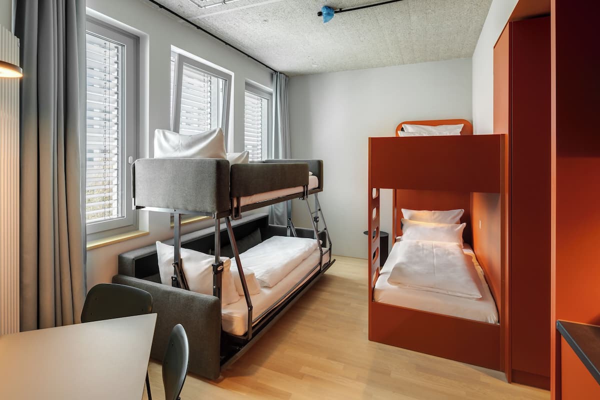 A compact hotel room with bunk beds, a small table, and a chair.
