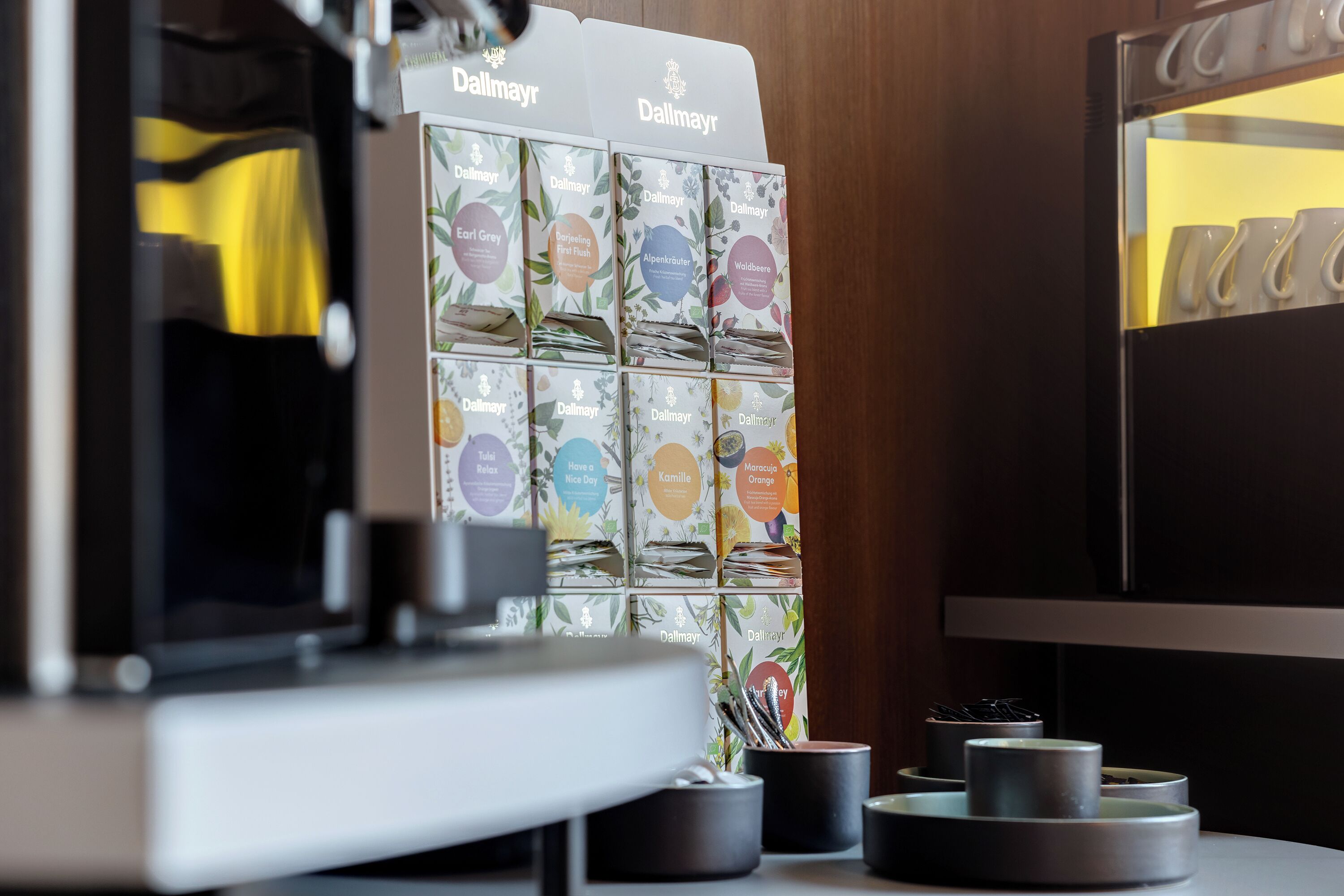 En kaffemaskin och ett utbud av kaffekapslar med etiketter som till exempel Earl Grey och Kamomill.