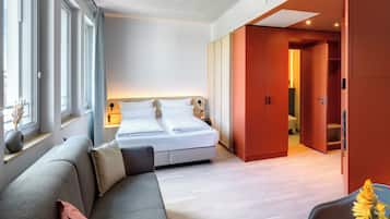 A modern hotel room with a bed, a sofa, and a bathroom visible through an open door.