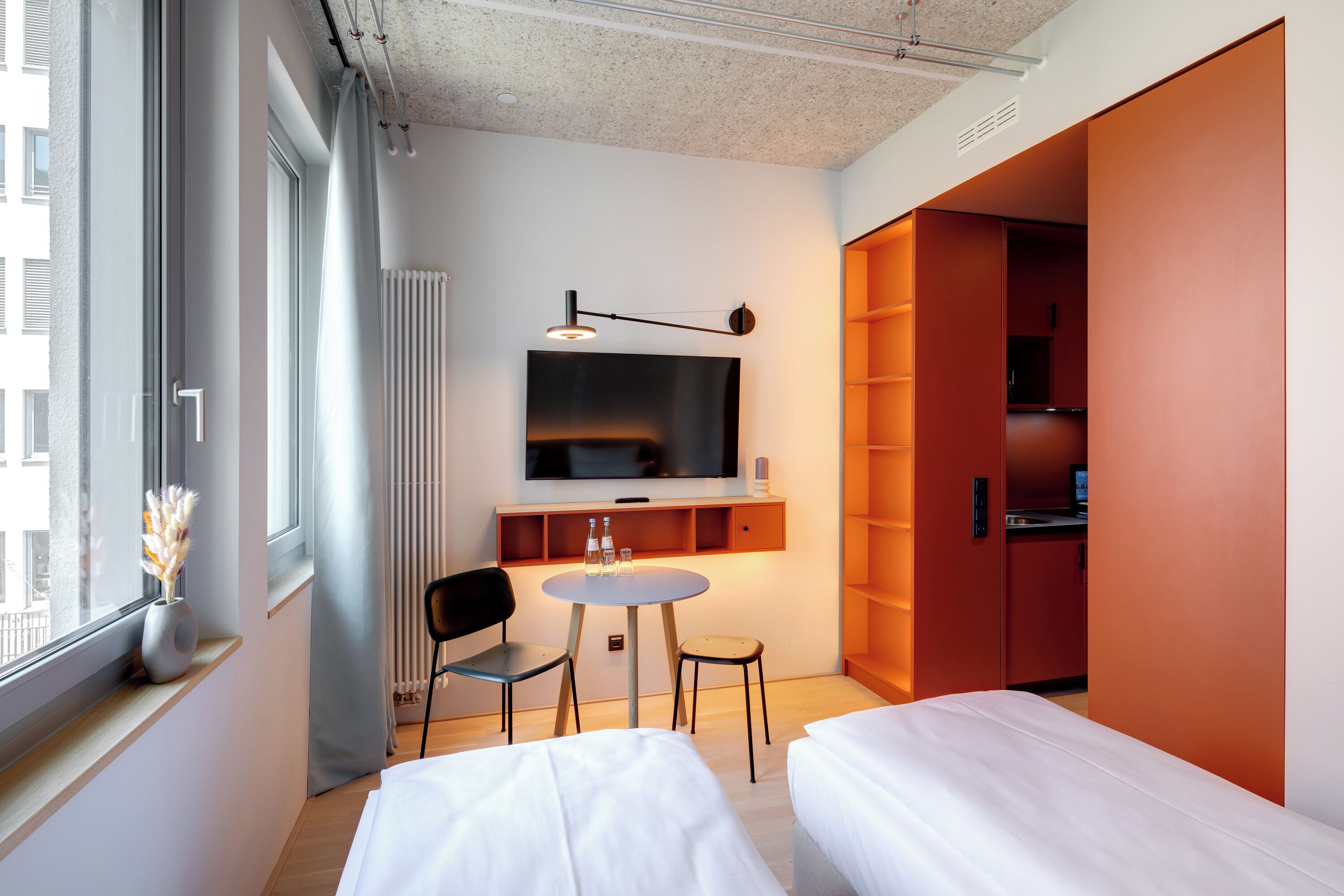 Habitación de hotel moderna con dos camas, televisión, una mesita con sillas y ventana con vista a la ciudad.
