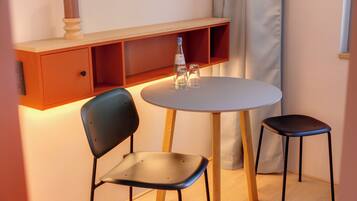 A small room with a round table, two chairs, a shelf with a candle, and a bottle.