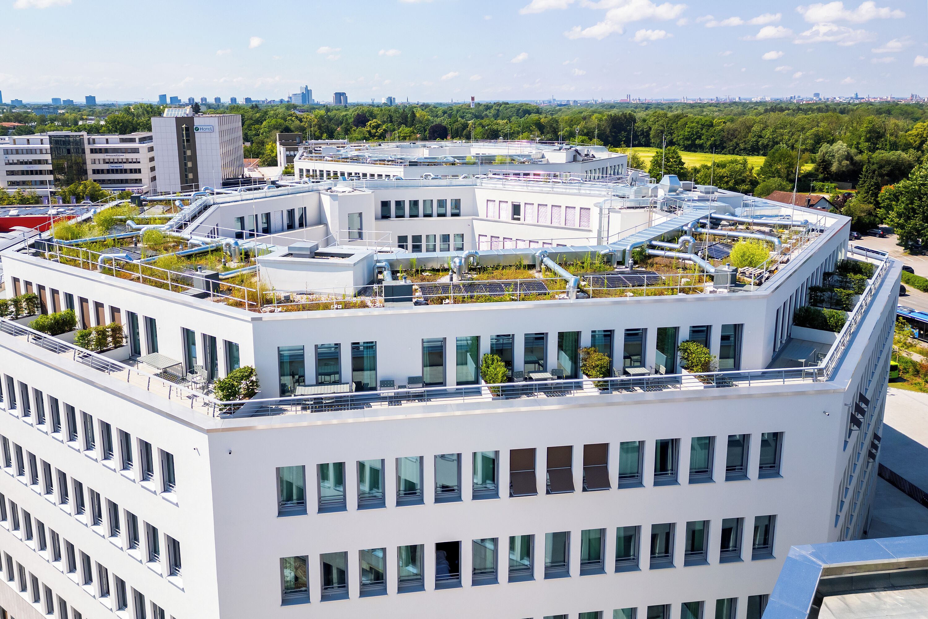 A modern building with multiple floors, large windows, and a rooftop garden.