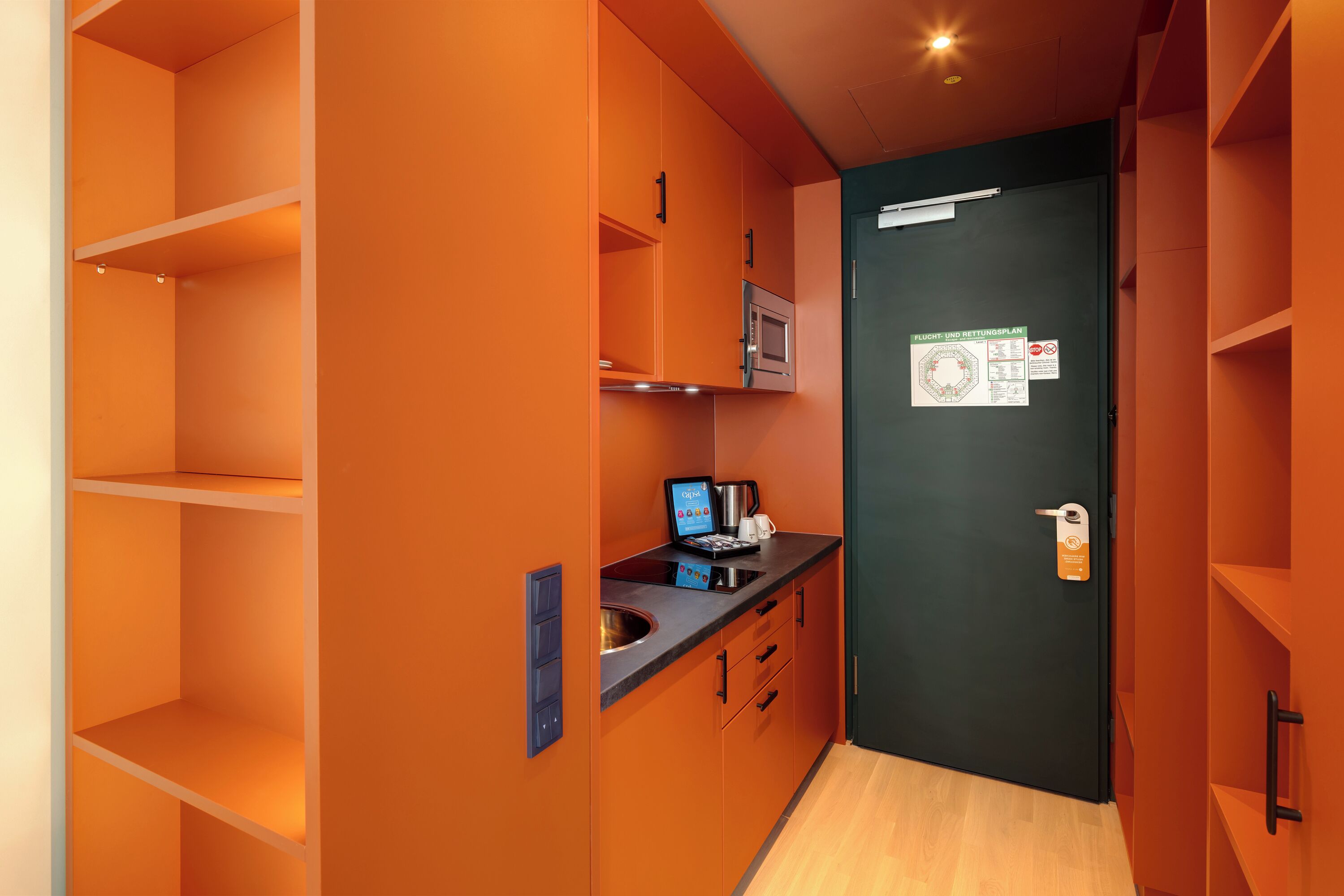 A compact kitchen with orange walls, a microwave, a coffee machine, and a small sink.