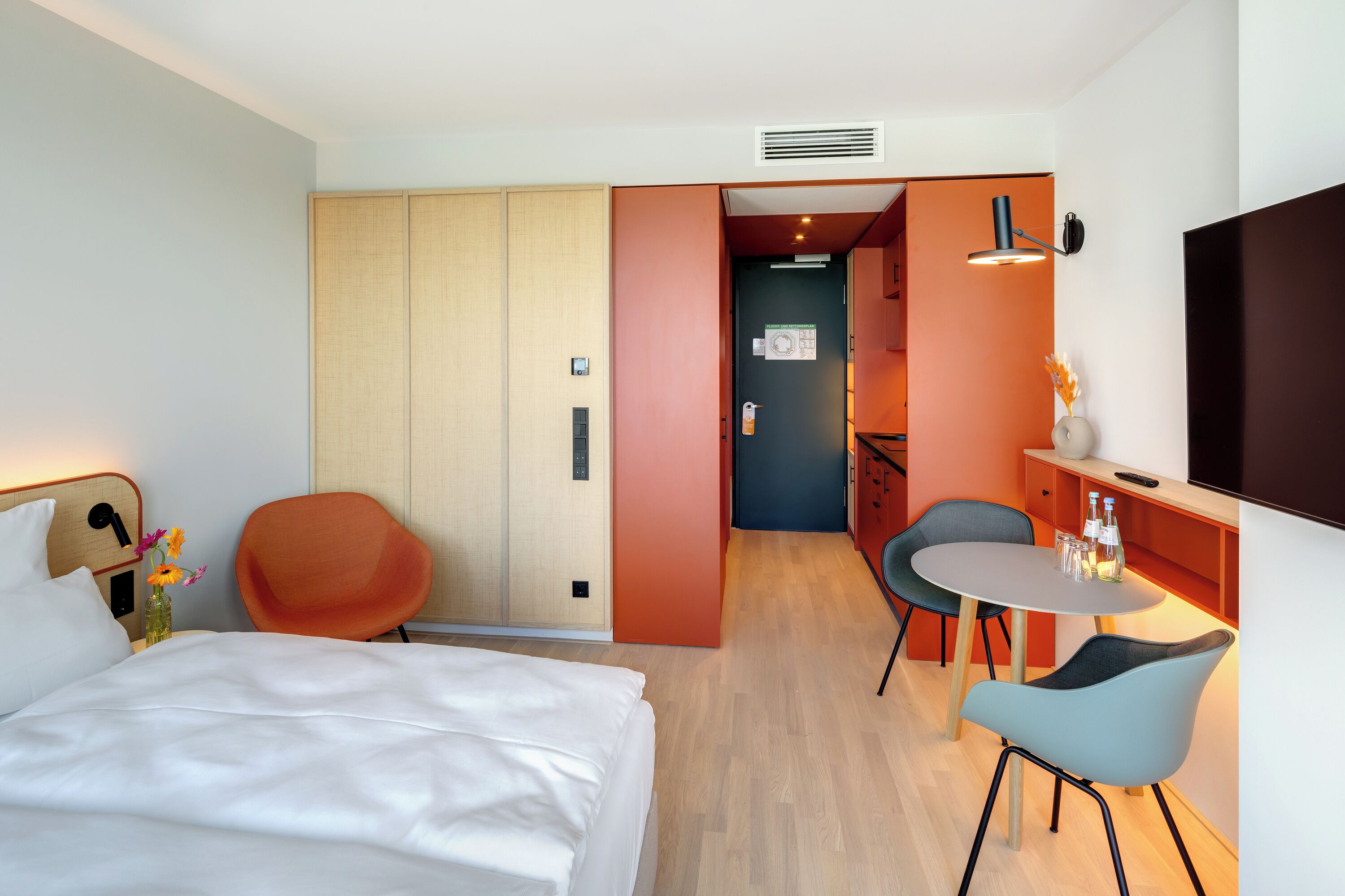A hotel room with a bed, a desk, two chairs, a TV, and a wardrobe.