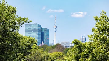 Un paisaje urbano con edificios modernos, incluyendo una torre destacada, rodeado de frondosos árboles verdes.