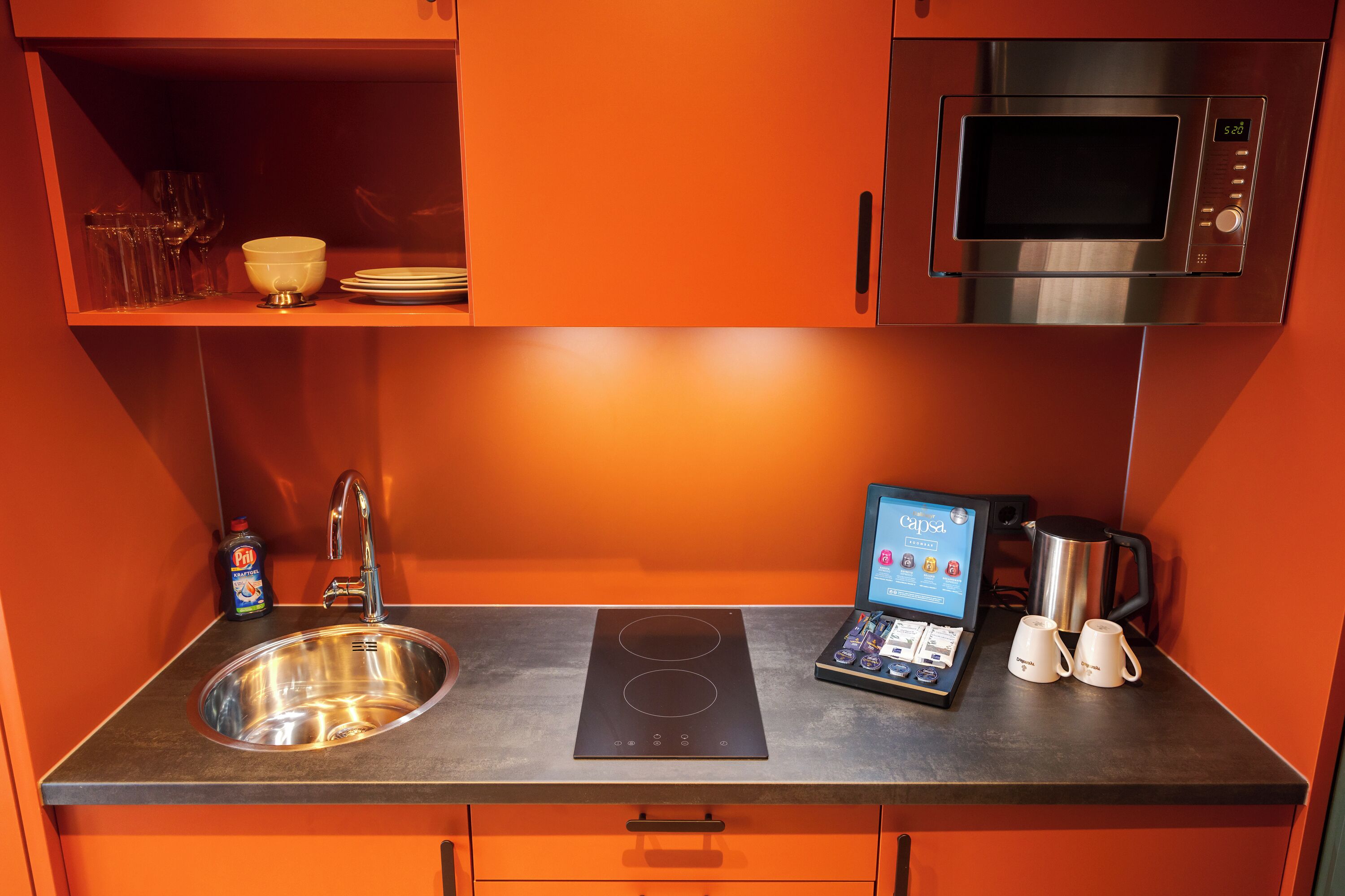 A compact kitchen with a stainless steel sink, a built-in induction cooktop, a microwave, and a coffee maker.