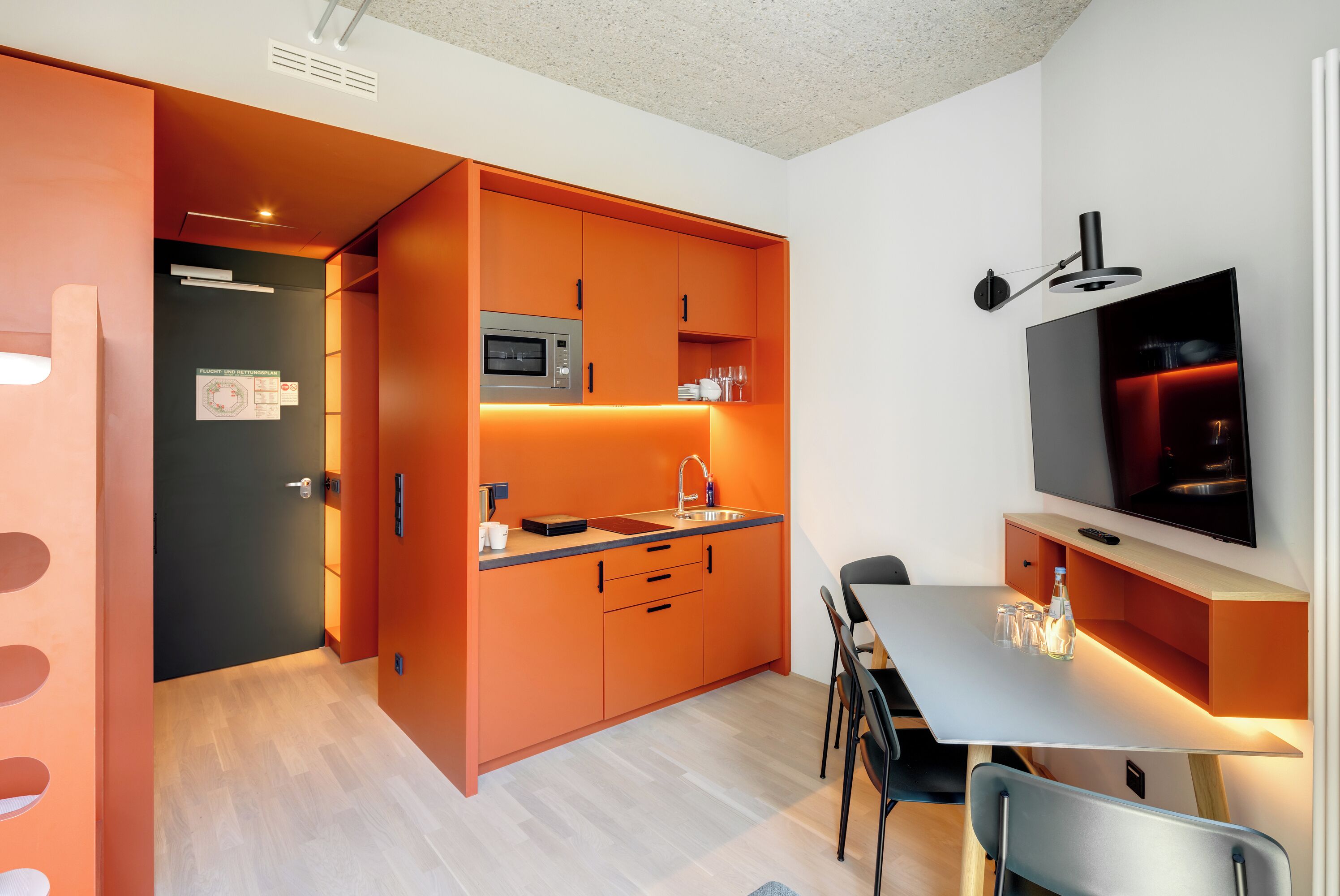 Ett modernt kök med orange köksinredning, en mikrovågsugn, en diskho och en matplats med ett bord och stolar.