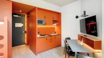 Ett modernt kök med orange köksinredning, en mikrovågsugn, en diskho och en matplats med ett bord och stolar.